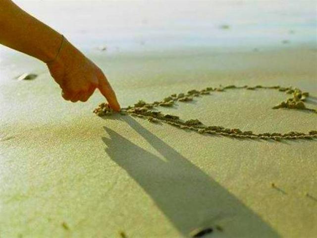 une main dessine un coeur dans le sable